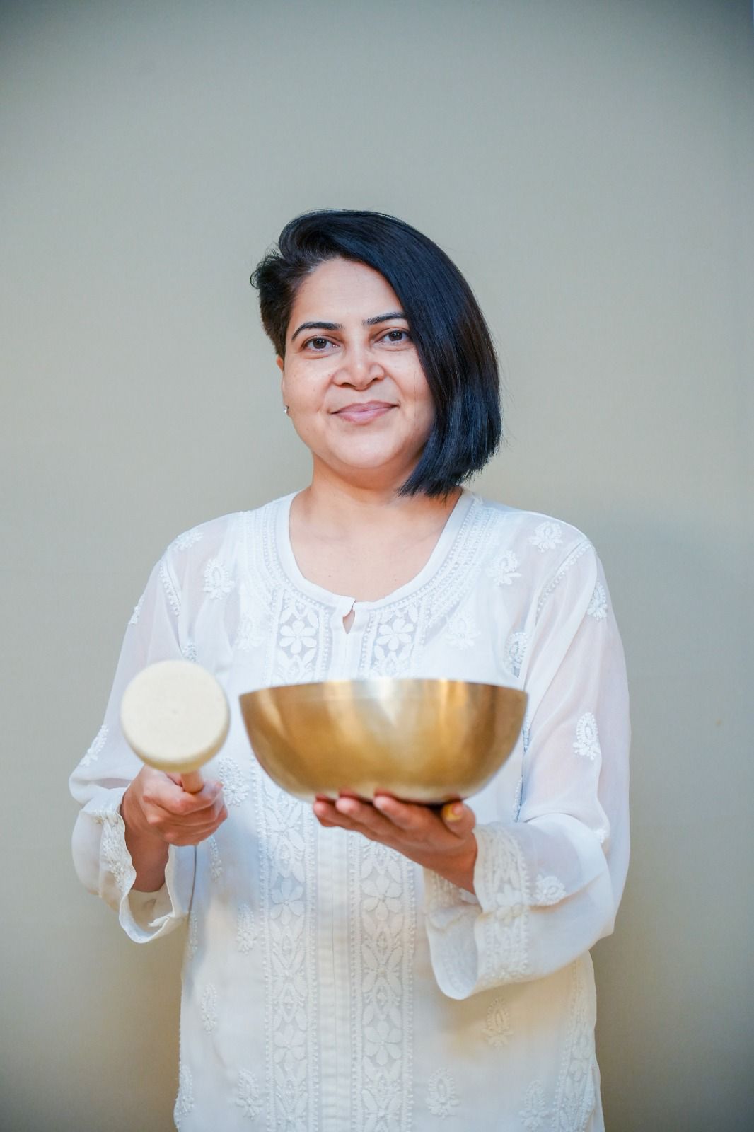 Vaishali Maa in a white chikankari kurta holding a golden singing bowl